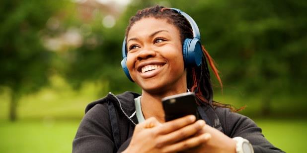 Ung kvinne med hodetelefoner og mobil, som hører på musikk i parken. Foto