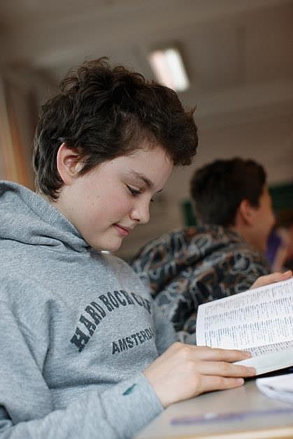 Bildet er tatt i et klasserom. Nærbilde av en gutt som leser i en bok. Illustrasjon
