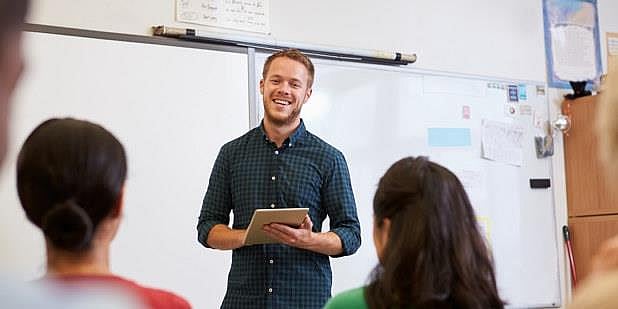 Foto av mannlig lærer som smiler og snakker foran elever