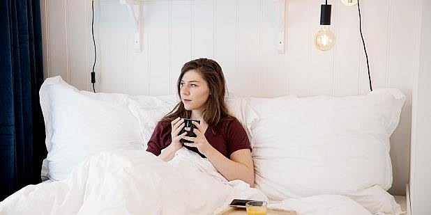 Dame i sengen med kaffekopp. Foto