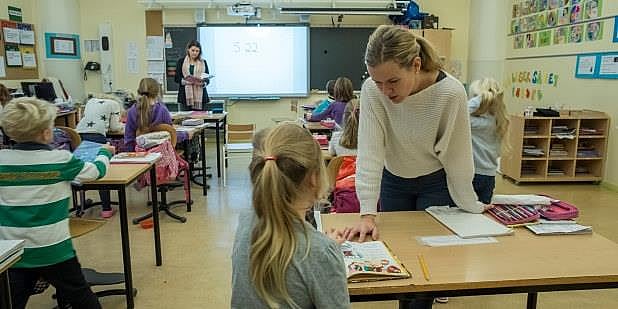 Bilde fra klasserom der en lærer hjelper en elev som sitter ved pulten sin.