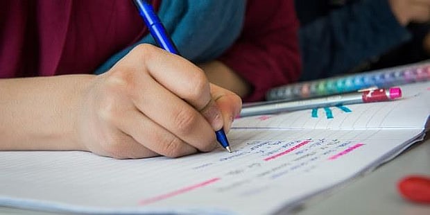 Bilde av hånden til en elev som skriver leksene sine i en skrivebok. Illustrasjonsfoto 