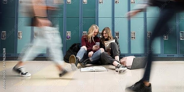 Elever som går fort gjennom skolekorridor mens andre sitter stille på gulvet. illustrasjonsfoto