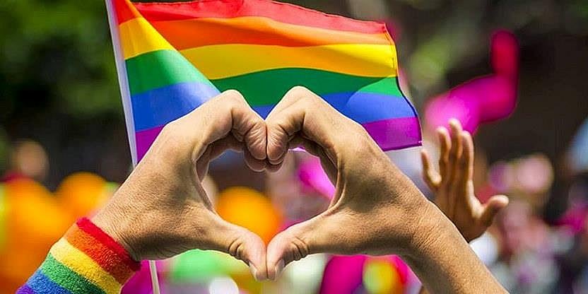 Prideflagg og to hender former et hjerte