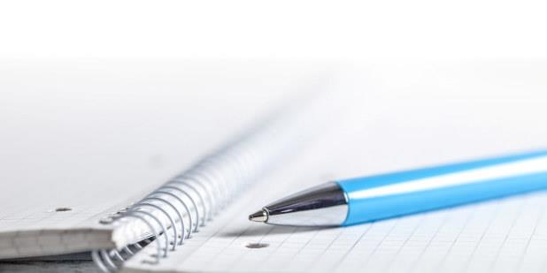 Nærbilde av en blå penn som ligger på en oppslått notatbok. Illustrasjonsfoto.
