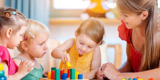 Tre barn som leker med klosser sammen med en barnehagelærer