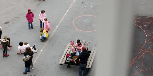 Skolegård sett i fugleperspektiv med barn som leker og noen som sitter ved en benk. Illustrasjonsfoto.