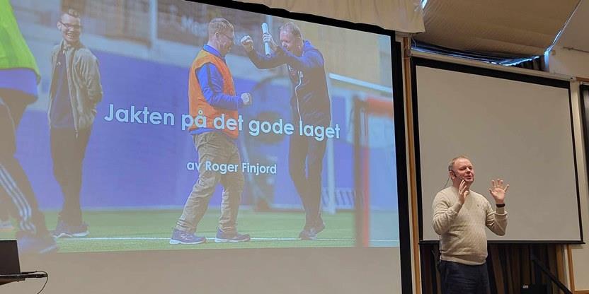 Foredragsholder Roger Finjord på scenen foran storskjermen som har teksten "Jakten på det gode laget". Foto