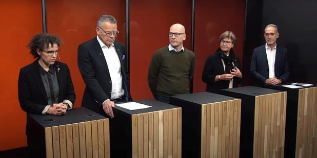 Bilde av fem personer som står ved hvert sitt bord i en paneldebatt.