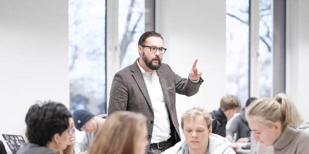 En mannlig lærer/lektor står foran elevene i klasserommet på en videregående skole og prater. Illustrasjonsfoto.