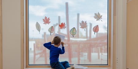Bildet viser en elev ved Oksenøya barneskole. Han sitter foran et vindu, og skriver på et ark.