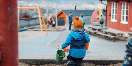 Uteområde i barnehagen, Noen barn, et par voksne, Sandkasse, Uteleke,r Ser litt av barnehagehuset.