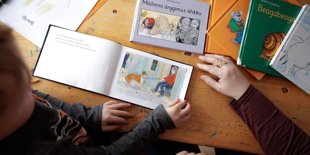 Samisk barnehage, barn leser barnebøker med barnehagelæreren. Flere bøker på bordet.