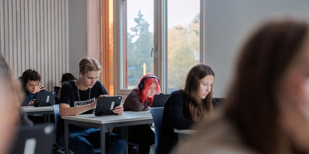 Foto av elever på ungdomsskole. De sitter i klasserommet og jobber konsentrert på ipad. Illustrasjonsfoto