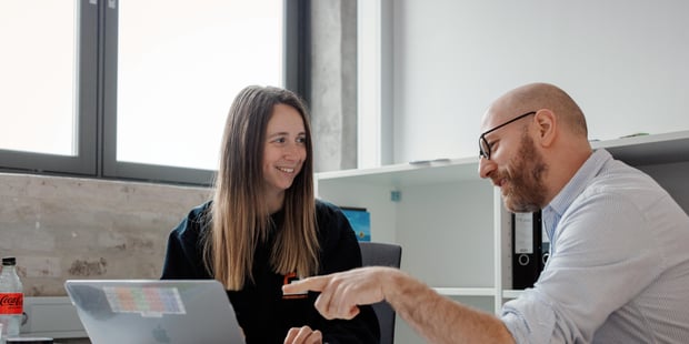 To lærere på arbeidsrom. Begge sitter ved pult med en PC.