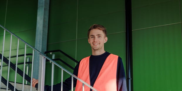 Bildet viser en lærer ved Oksenøya barneskole. Han står i en trapp med en oransje refleksvest mens han smiler.
