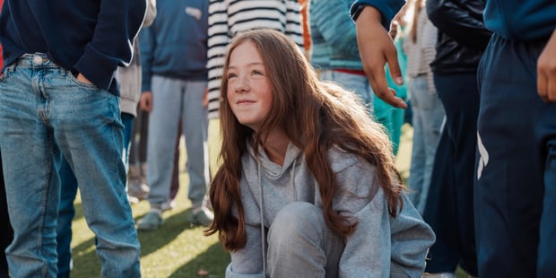 Bilde av en jente ca 12 år i skolegården som sitter på huk og titter opp.