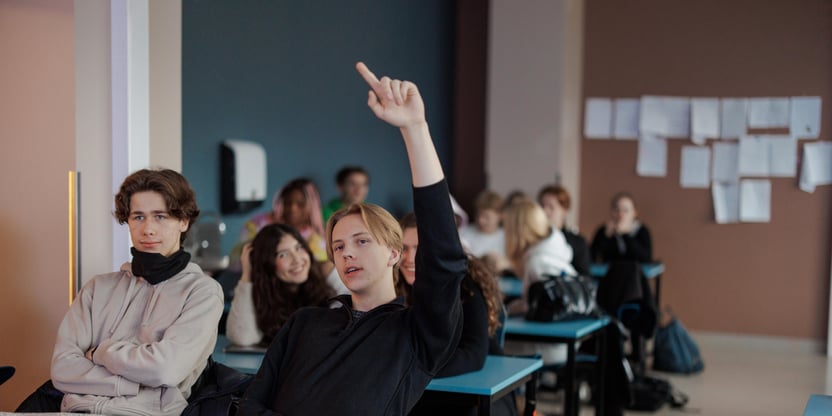 Foto av elev som rekker opp hånd i klasserom