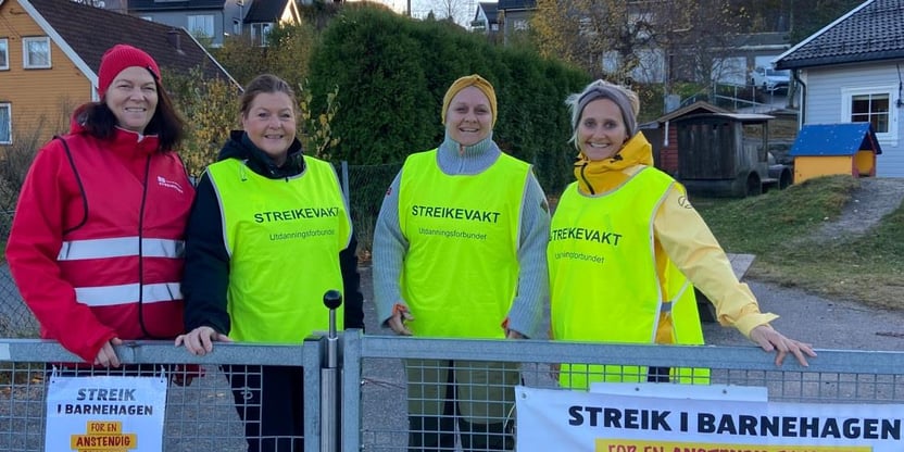 Bilde av 4 streikende i Strai barnehage. De har streikevester, banner og plakater.
