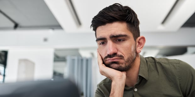 Trist, forretningsmann og jobber på et kontor på bærbar PC, skrivebord og arbeidsplass med tretthet, sliten energi og utbrenthet. Deprimert, konsulent og arbeid på datamaskin med angst for tilbakemeldinger eller prosjekt e-post