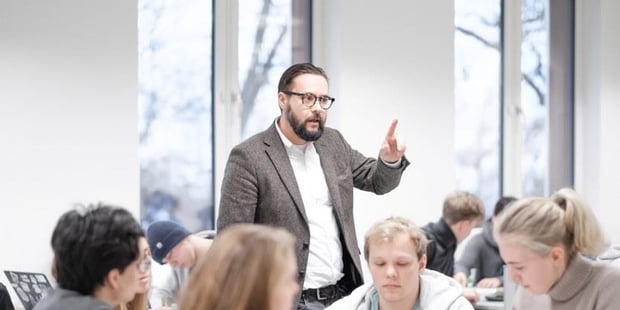 Lærer peker og forklarer midt i et klasserom