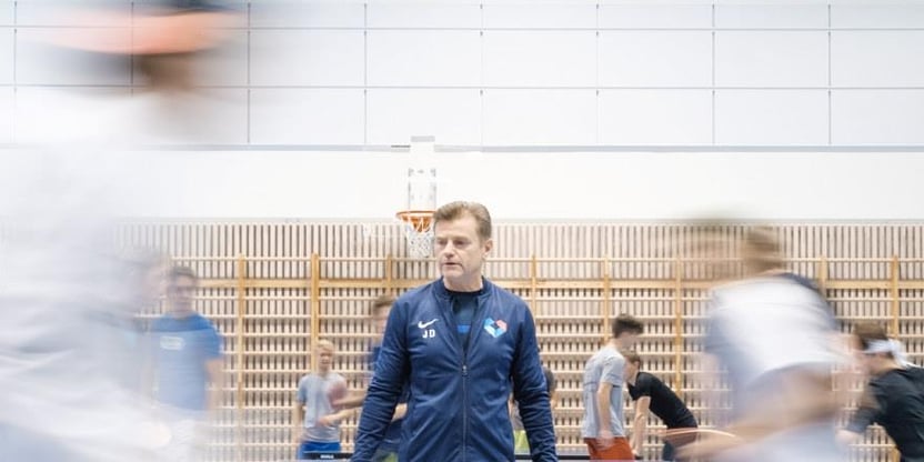 Lærer som står i en gymsal med elever i bevegelse. Illustrasjonsbilde. 