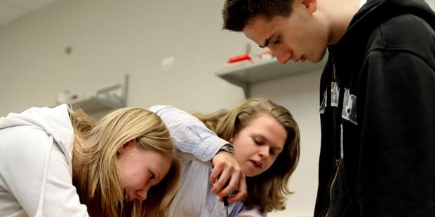 To personer skrur på noe, mens en tredje person ser på. Foto.