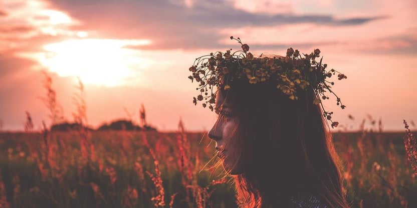 Profilbilde av en person (kvinne ) med blomsterkrans i håret. Ser solnedgangen i bakgrunnen. Illustrasjonsbilde