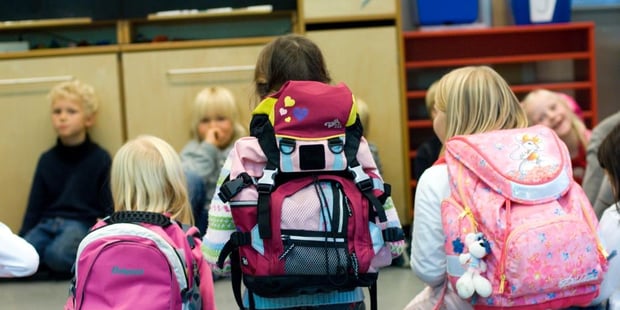 Barn som sitter i en ring på et gulv. Noen med ransel på. Foto.