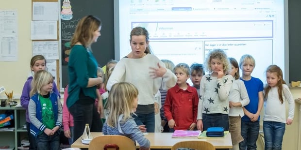En gjeng barn står samlet med en voksen person foran seg. Foto. 