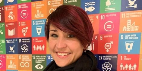 Bilde av Ann Mari Milo Lorentzen foran en plakat av bærekraftsmålene på FNs kvinnekonferanse i New York