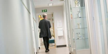 Ansatt på en skole går nedover en korridor. Vi ser personen bakfra. Illustrasjonsfoto