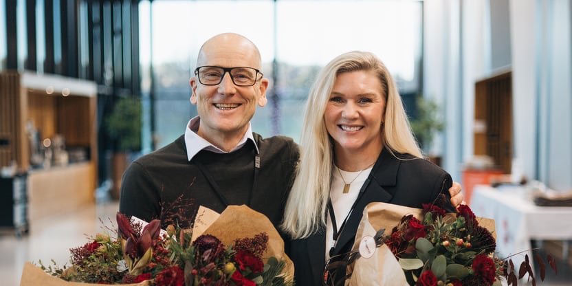 Mann og kvinne står med blomsterbukett i hendene og ser smilende mot fotografen.