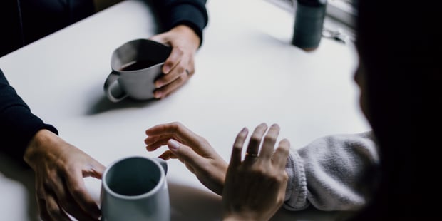 Bildet viser to personer som prater over en kaffekopp. De sitter ved et bord, men du ser bare hendene til de to personene.