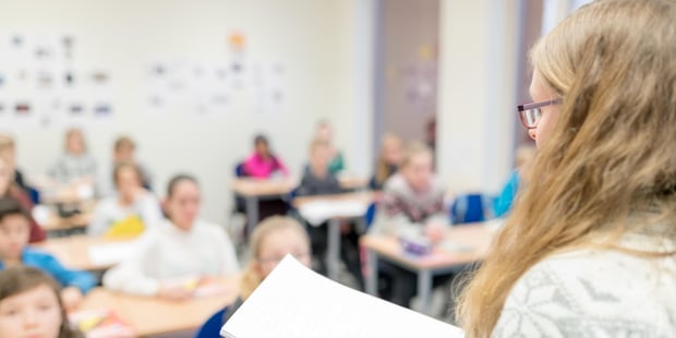 Bildet viser en kvinnelig lære bakfra. Hun står foran noen få elever i et klasserom.