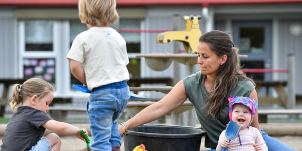 Foto av kvinnelig barnehagelærere som sitter og leker med tre barn