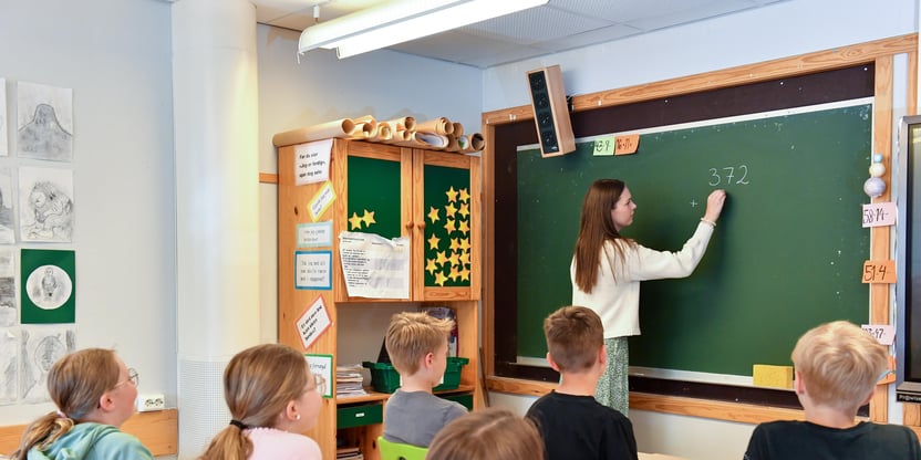 Lærer skriver på tavle mens elever ser på.