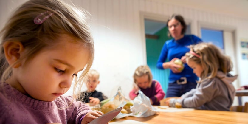 Barn i aktivitet i en barnehage, jente i forgrunnen, flere barn og voksen i bakgrunnen. FOTO.