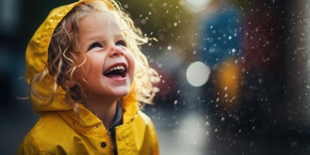 Liten jente i gul regnfrakk smiler i regnet