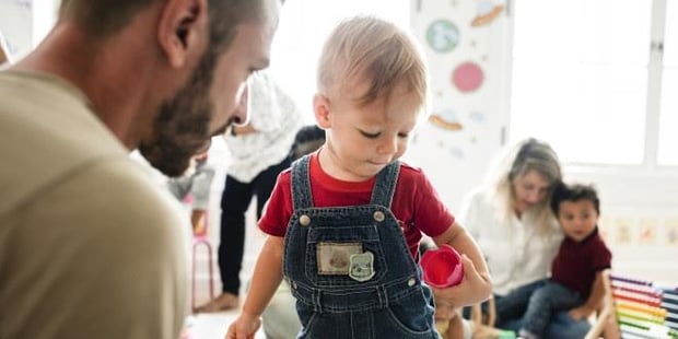 Mannlig barnehagelærer med liten gutt. I bakgrunnen kvinnelig barnehagelærer med gutt på fanget. Illustrasjonsfoto