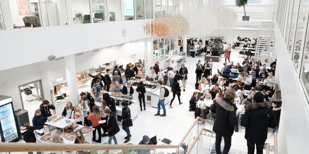 Mange unge mennesker i en stor hall, mange med ryggsekker. Foto. 