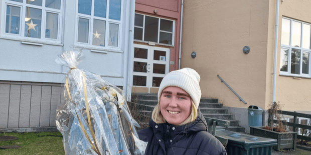 Bilde er av Eline Larsen utenfor Furulunden skole med gave hun fikk fra lokallaget, sekk, blomst og bag.