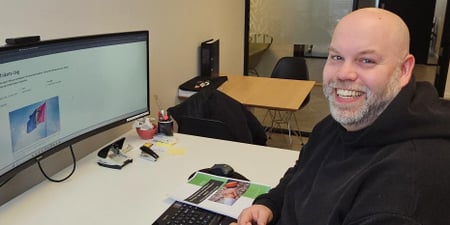 Bilde av Bjørn Martinsen sittende foran sin pc, med bilde av arrangement fra Universtitet i Innlandet på samenes nasjonsaldag