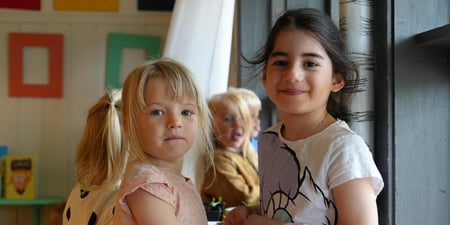To jenter leker i en barnehage og smiler mot kamera