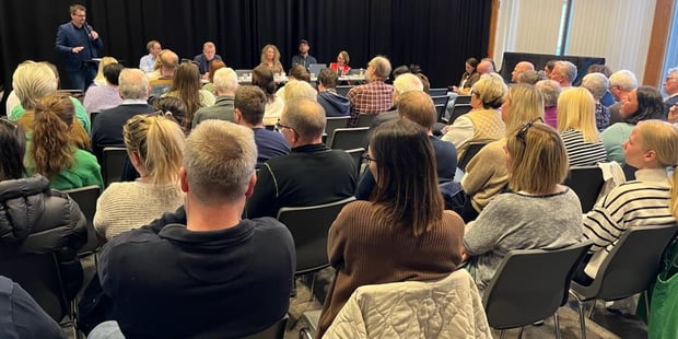 Bilde av publikum bakfra og politikerne foran sittende ved et bord. 