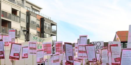 Mange mennesker står sammen med plakater på pinner over hodet