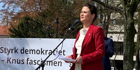 Kvinne som står på talerstol ute i solskinn.