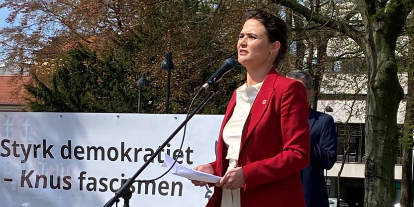 Kvinne som står på talerstol ute i solskinn.