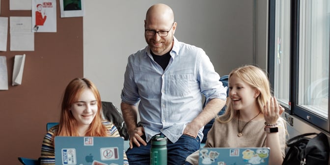 Mannlig lærer sammen med to elever i klasserom, videregående skole.