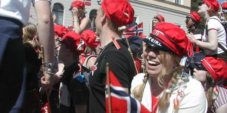 Foto av glad kvinnelig russ foran slottet på 17. mai med norsk flagg.